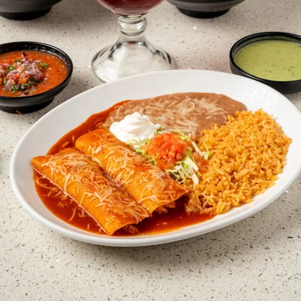 Two enchiladas with red sauce, rice, refried beans, and sour cream on a white plate.