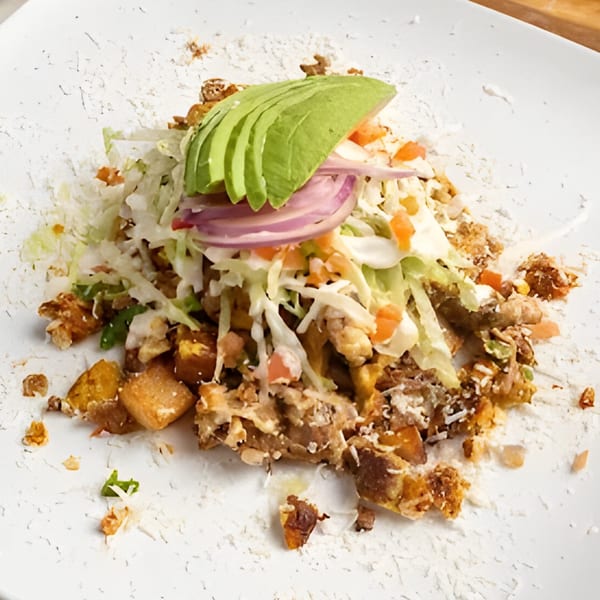 Mexican dish with meat, potatoes, shredded lettuce, red onion, avocado slices, and cheese.