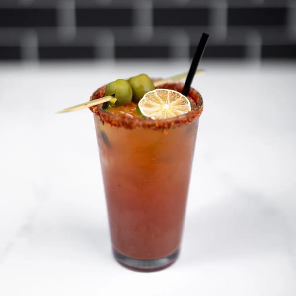 A Bloody Mary cocktail with a chili-lime rim, garnished with green olives and a dried lime slice.