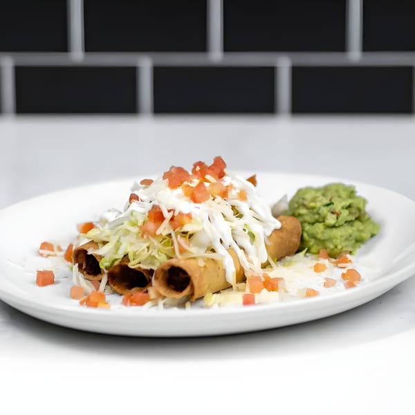 Crispy taquitos topped with shredded lettuce, diced tomatoes, sour cream, and a side of guacamole.