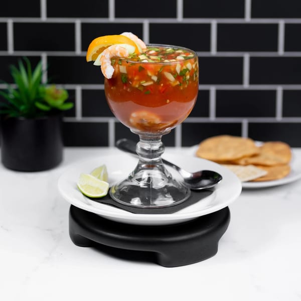 Shrimp cocktail in a goblet with lime wedges and tortilla chips on a white marble counter.