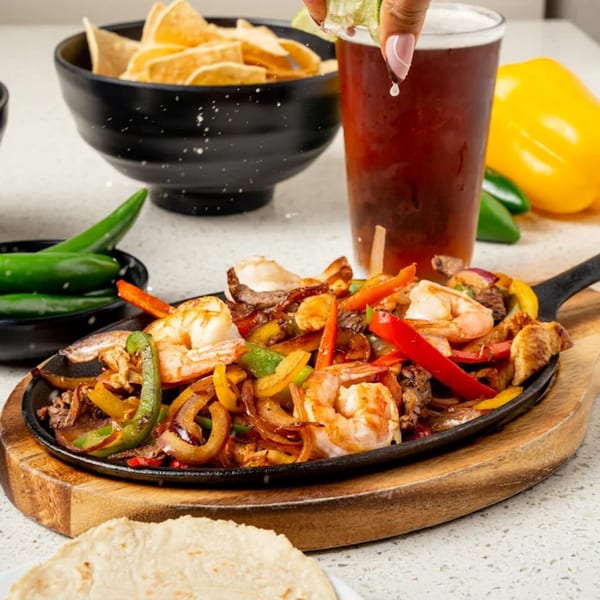 Sizzling fajitas with shrimp, steak, colorful peppers, and onions, served with tortillas, chips, and a beer.