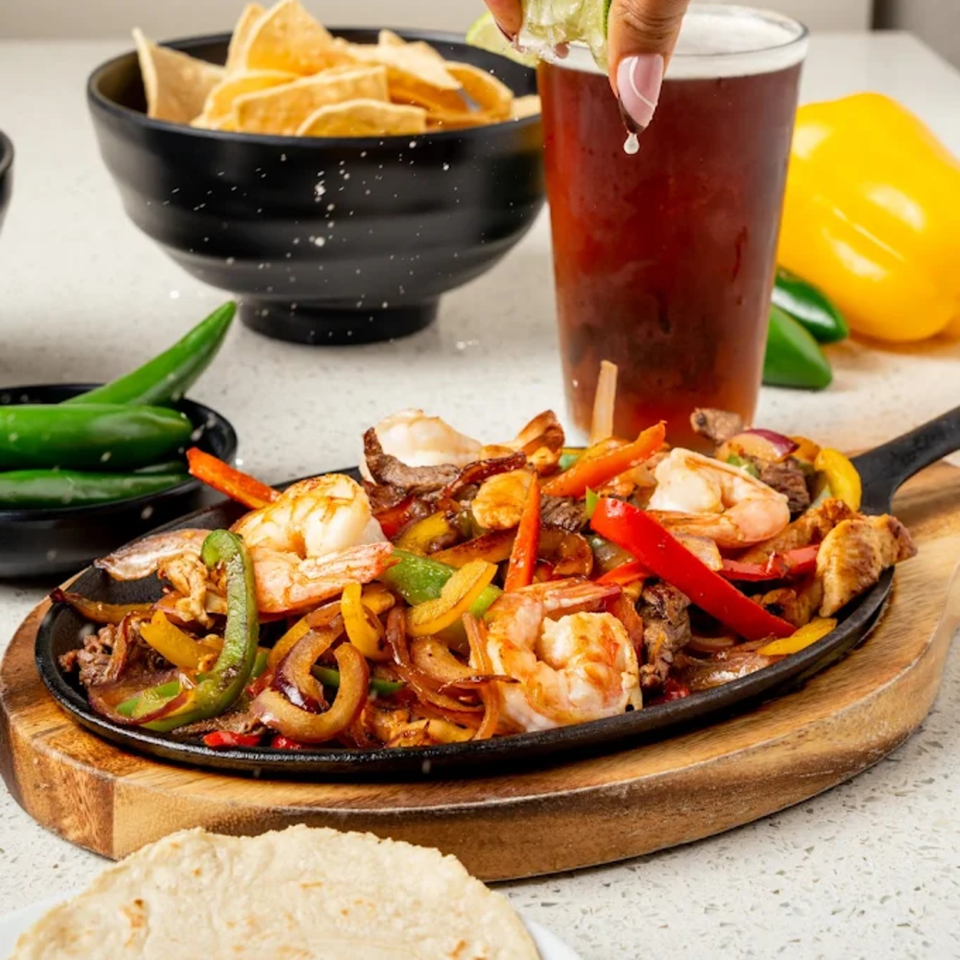 Sizzling fajitas with shrimp, steak, colorful peppers, and onions, served with tortillas, chips, and a beer.