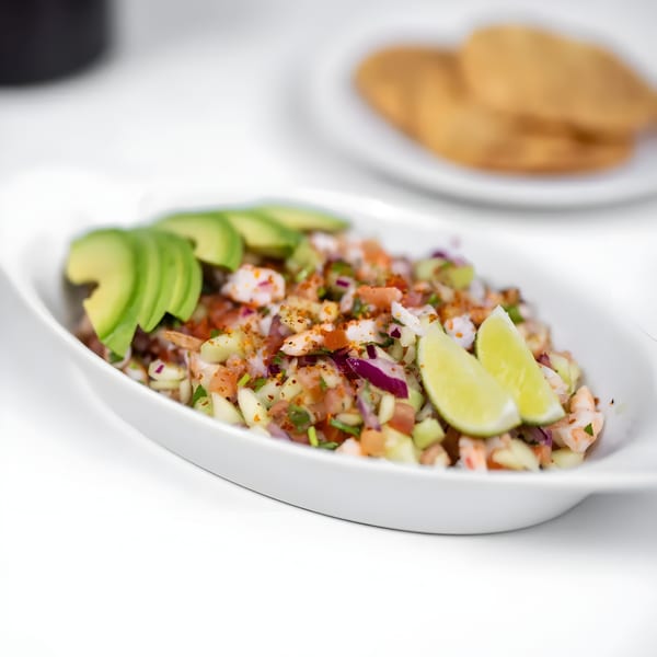 Mexican shrimp ceviche with avocado, lime, and spices in a white bowl, with tostadas in the background.