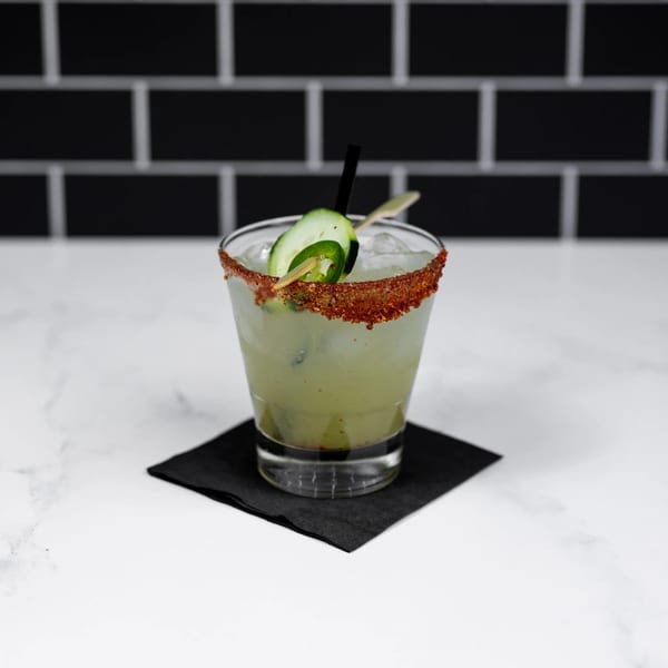 A green Margarita's Cocina y Cantina cocktail with a chili-lime rim, cucumber, and jalapeño garnish.