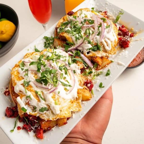 Two fried eggs with sour cream, red onions, and cilantro on a bed of potatoes and chorizo.
