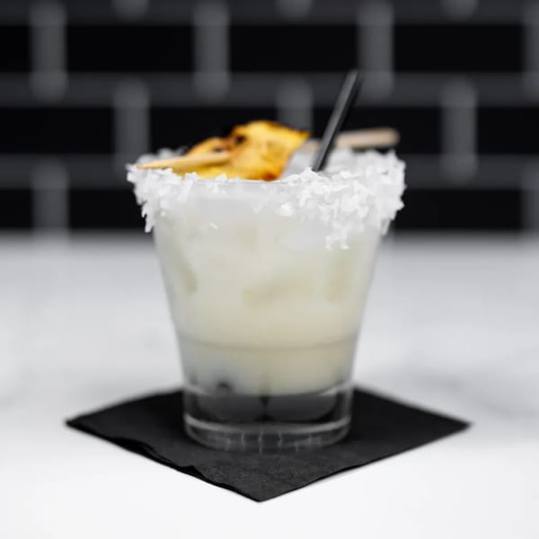 Coconut margarita with a pineapple garnish and black straw, on a black napkin.