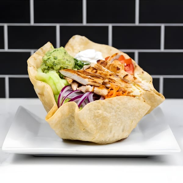 A taco salad with grilled chicken, guacamole, sour cream, and vegetables in a crispy tortilla bowl.