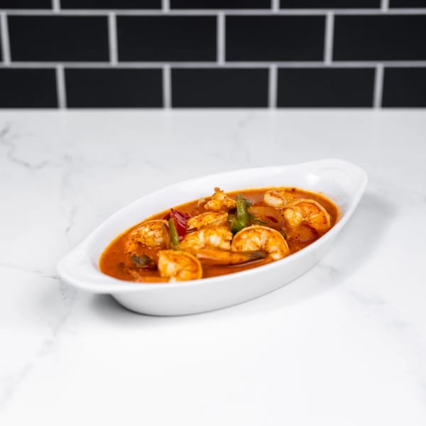 Shrimp in a rich red sauce with peppers and onions, served in a white oval dish.